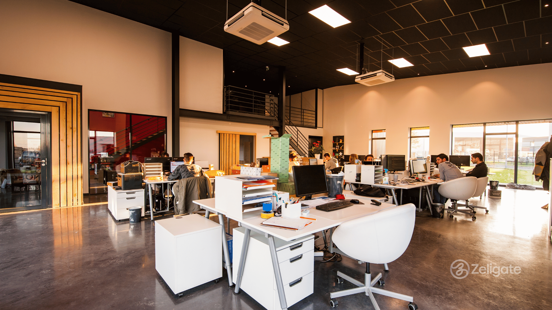 Modern open-plan office with multiple employees working at desks and collaborating in a bright workspace.
