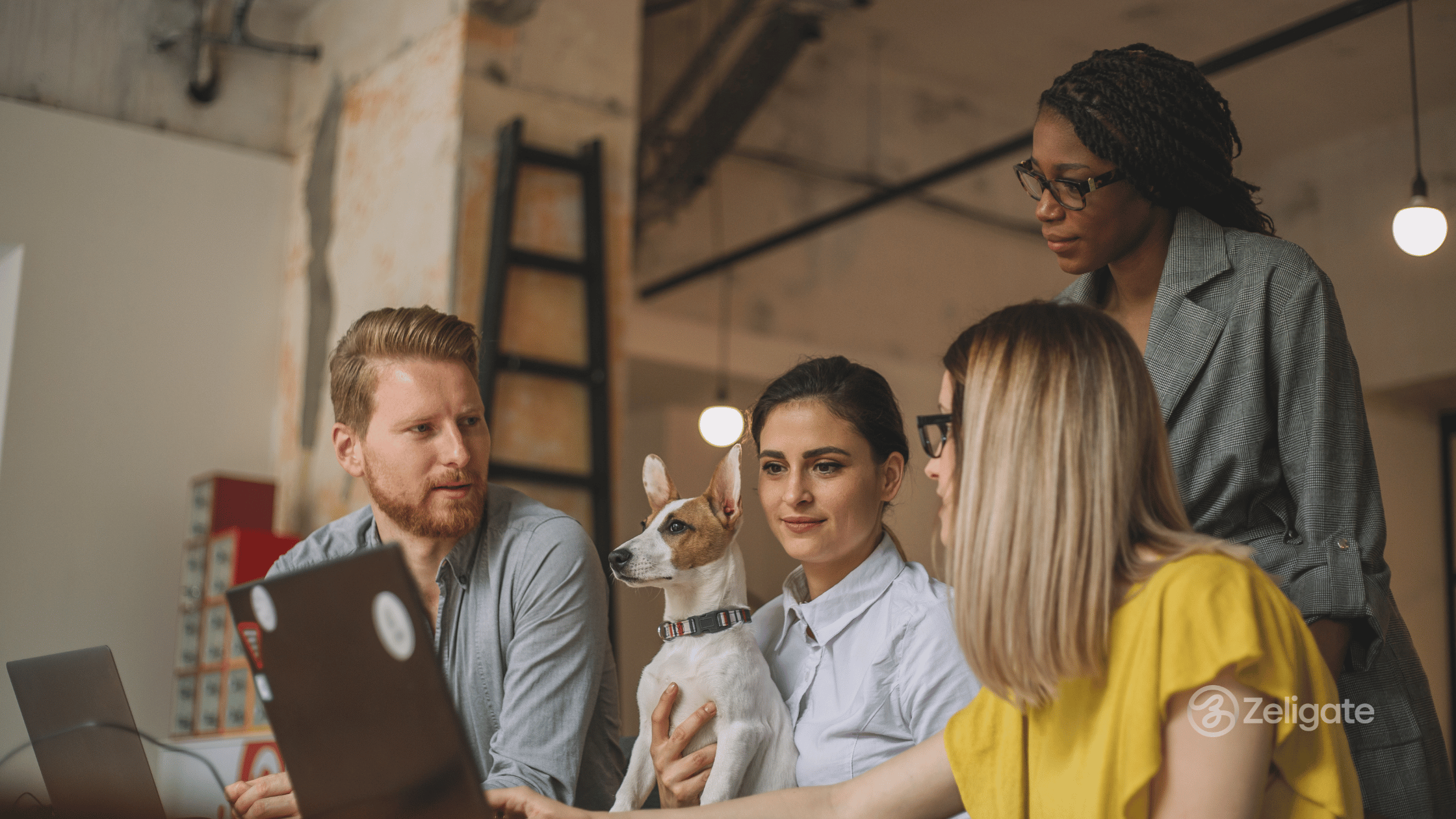 Diverse group of professionals collaborating around laptops in a casual office setting, with a dog sitting on one team member’s lap, representing teamwork and innovative hiring culture.
